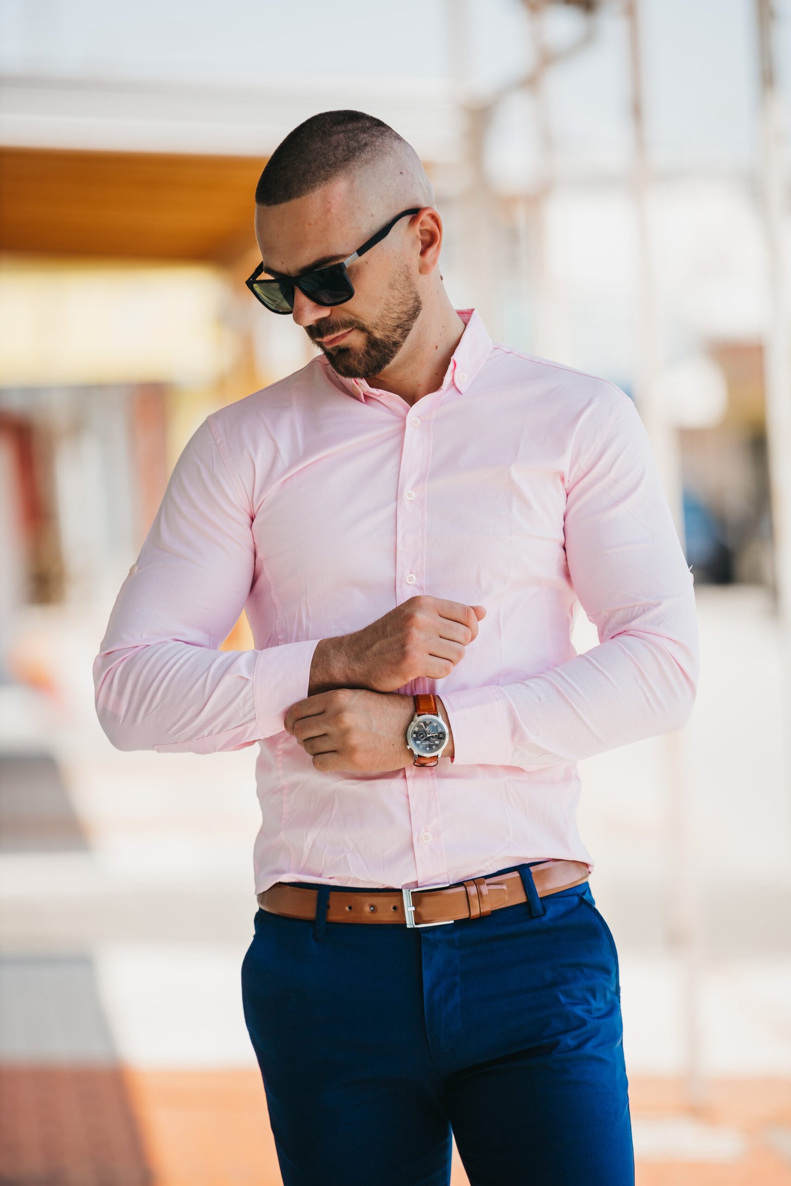 A cool handsome Caucasian man wearing an elegant light pink shirt and sunglasses posing outdoor
